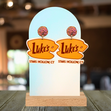 Load image into Gallery viewer, A cafe background with earrings displayed that feature the “Luke’s Diner” logo from Gilmore girls