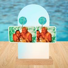 Load image into Gallery viewer, A pool background with a pair of New Girl earrings featuring Tran holding Nick Miller in the pool as he cringes