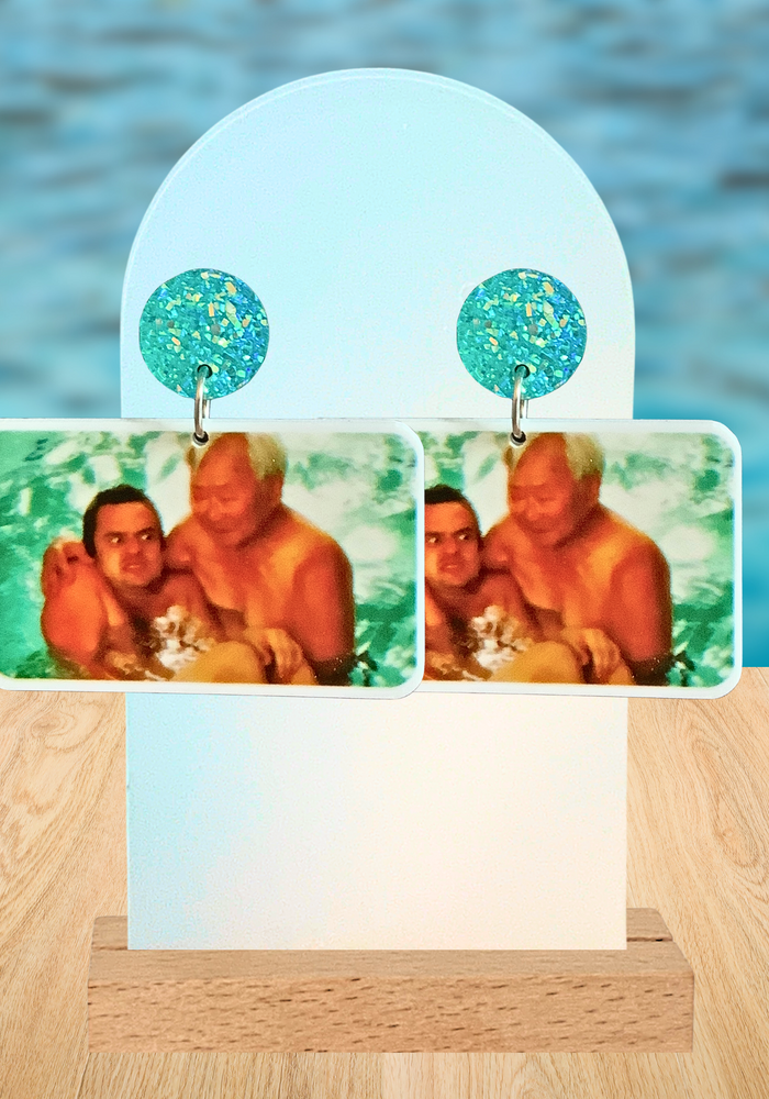 A pool background with a pair of New Girl earrings featuring Tran holding Nick Miller in the pool as he cringes