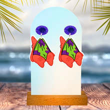 Load image into Gallery viewer, Dangling Patrick Star earrings on an earring display in front of an oceanic backdrop