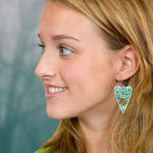 Load image into Gallery viewer, A blonde model wearing a pair of aqua blue translucent Ouija planchette earrings, perfect for adding a fun and mystical touch to your Halloween look.