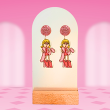 Load image into Gallery viewer, Earrings featuring animated Lizzie Mcguire with a boa and platforms, complete with pink studs and a pink background