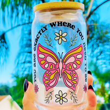 Load image into Gallery viewer, A 16 oz glass cup featuring a UVDTF wrap with a pink butterfly, daisies, and the phrase “You’re Exactly Where You Need To Be.” Comes with a bamboo lid and reusable glass straw. BPA-free and handwash only.