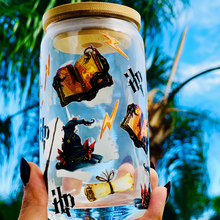 Load image into Gallery viewer, A 16 oz glass cup featuring a Harry Potter-inspired UVDTF wrap with wands, spellbooks, lightning bolts, and the Sorting Hat. Includes a bamboo lid and reusable glass straw, perfect for cold drinks. BPA-free and handwash only.
