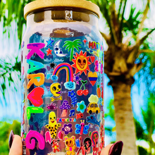 Load image into Gallery viewer, A 16 oz glass cup with a colorful Karol G-inspired UVDTF wrap featuring vibrant symbols, designs, and playful details. Includes a bamboo lid and reusable glass straw, perfect for cold drinks. BPA-free and handwash only.