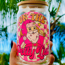 Load image into Gallery viewer, A 16 oz glass cup featuring a festive pink Santa design with the phrase "On The Petty List." Includes a bamboo lid and reusable glass straw, perfect for cold drinks. BPA-free and handwash only.