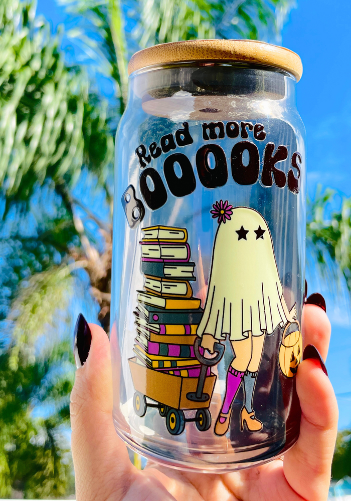 A 16 oz glass cup featuring a cute ghost design pulling a wagon full of books with the text