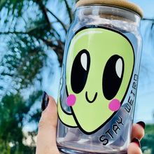 Load image into Gallery viewer, A 16 oz glass cup featuring a cute green alien design with the words "Stay Weird," paired with a bamboo lid and reusable glass straw. Perfect for quirky drinkware lovers and iced coffee enthusiasts.