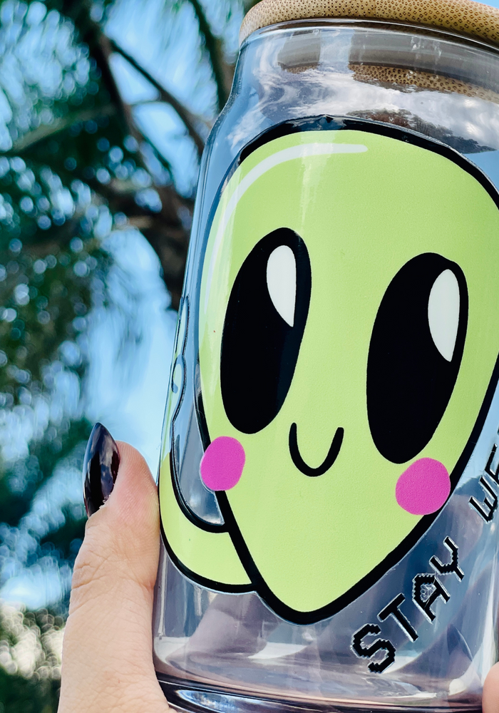 A 16 oz glass cup featuring a cute green alien design with the words
