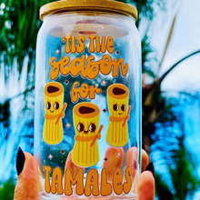 Load image into Gallery viewer, A 16 oz glass cup featuring a cute tamale-themed UVDTF wrap with the phrase “’Tis the Season for Tamales.” Includes a bamboo lid and reusable glass straw, perfect for cold drinks. BPA-free and handwash only.