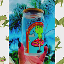 Load and play video in Gallery viewer, A 16 oz glass cup featuring a colorful UVDTF wrap with a smiling frog on a mushroom under a rainbow and the text “It’s Gonna Be Okay.” Comes with a bamboo lid and reusable glass straw. BPA-free and handwash only.