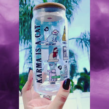 Load and play video in Gallery viewer, A 20 oz glass cup featuring colorful cat illustrations and Taylor Swift album-inspired designs, with the phrase "Karma is a Cat," paired with a bamboo lid and glass straw. Perfect for Swifties and cold drink lovers.