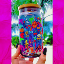 Load and play video in Gallery viewer, A 16 oz glass cup with a colorful Karol G-inspired UVDTF wrap featuring vibrant symbols, designs, and playful details. Includes a bamboo lid and reusable glass straw, perfect for cold drinks. BPA-free and handwash only.