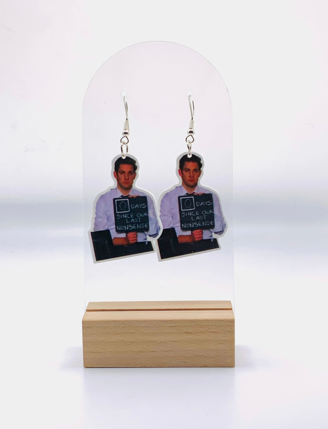 A pair of earrings featuring a depiction of Jim Halpert from The Office holding a sign that reads '0 days since last nonsense,' capturing the humorous essence of the character and the show's witty banter.