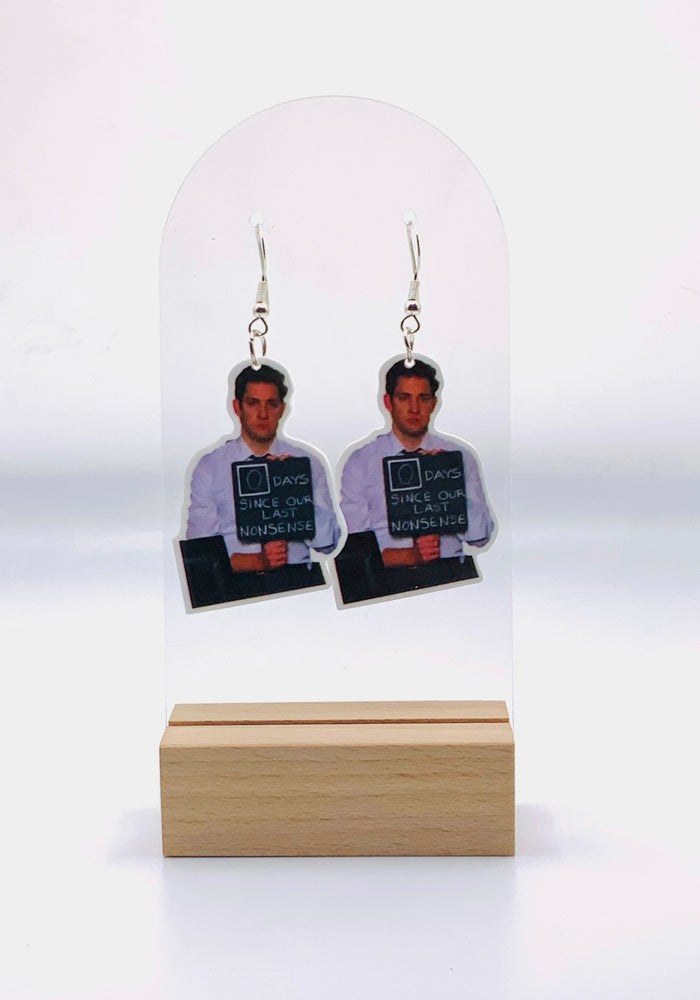 A pair of earrings featuring a depiction of Jim Halpert from The Office holding a sign that reads '0 days since last nonsense,' capturing the humorous essence of the character and the show's witty banter.