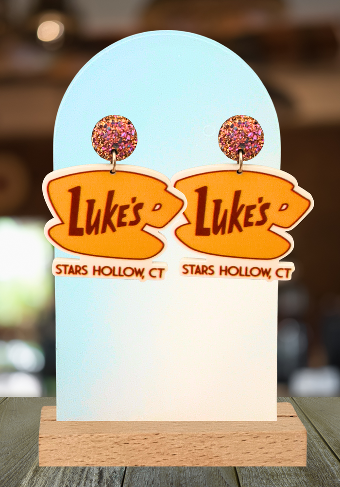 A cafe background with earrings displayed that feature the “Luke’s Diner” logo from Gilmore girls