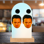 A bar background with a pair of New Girl earrings featuring Nick Miller’s grumpy frowning face