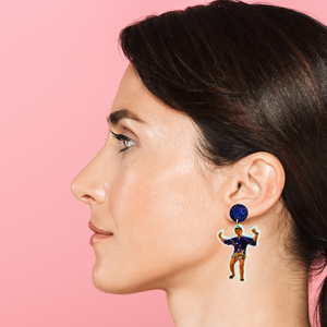 A woman against a pink backdrop wearing earrings featuring Schmidt from New Girl posing in a kimono 