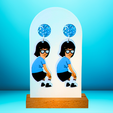 Load image into Gallery viewer, Earrings against a bright blue backdrop featuring Tina Belcher from Bob’s Burgers dancing
