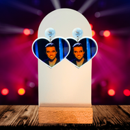Stage background with heart shaped earrings at the forefront featuring a close up of Mac as the Nightman from Always Sunny in Philadelphia