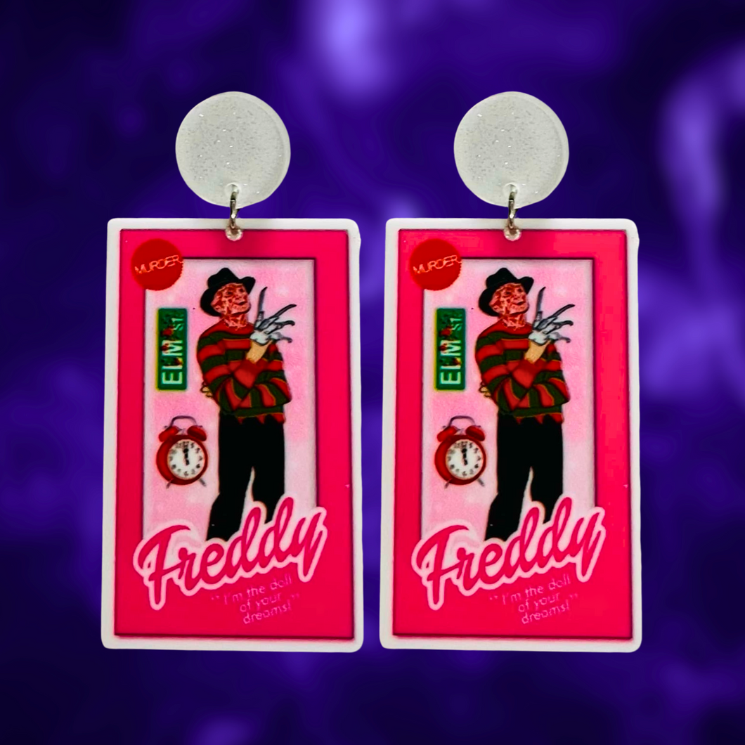 Earrings featuring Freddy Krueger in a Barbie-style box, with an Elm Street sign and alarm clock, ideal for fans of horror movies and playful Halloween fashion.