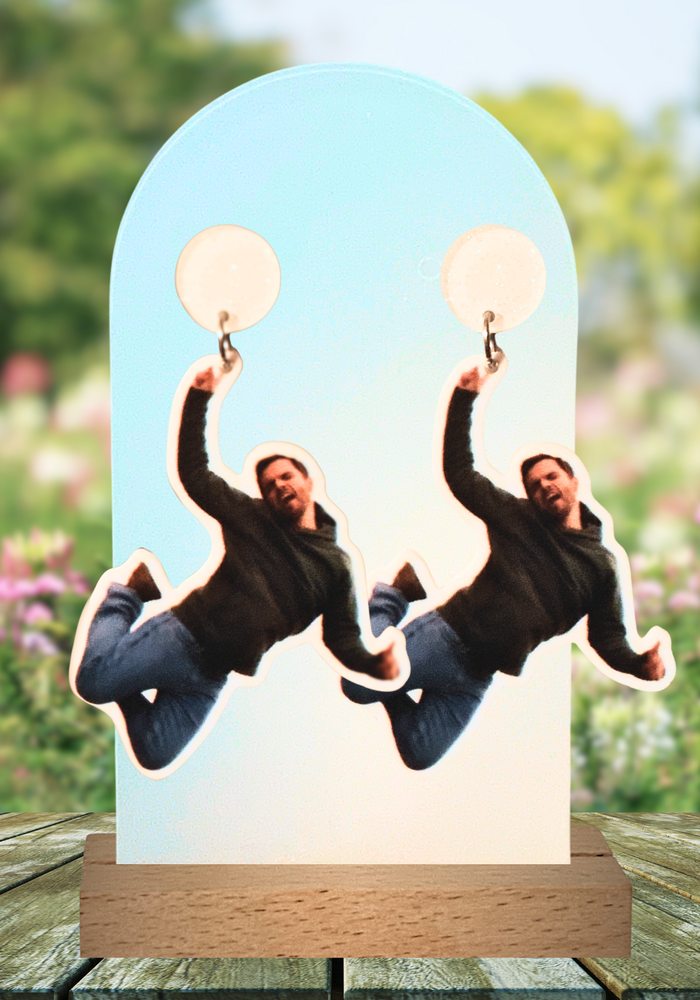 Earrings on a garden table featuring Nick Miller jumping up in the air, from his infamous “Freeze Frame” New Girl moment