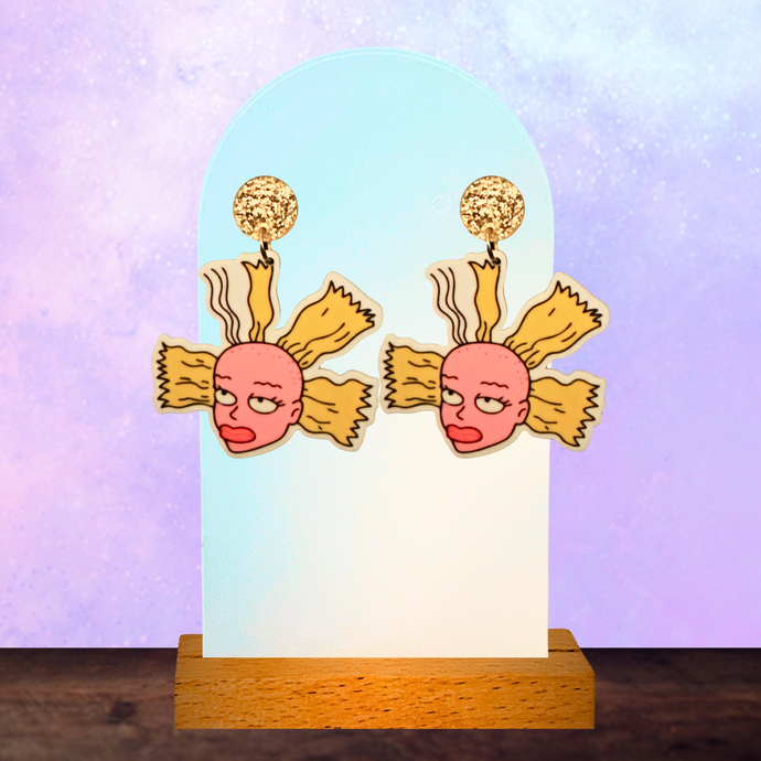 An earring stand with Cynthia doll head earrings from Rugrats on a purple background

