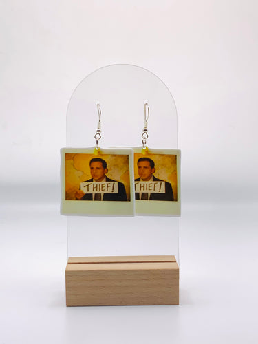 Earrings featuring the infamous Polaroid snapshot of Michael Scott from 'The Office' on the Chinese restaurant’s Wall of Shame. Each earring captures the moment Michael tried to skip the bill, humorously labeled with 'Thief'.