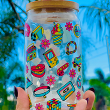 Load image into Gallery viewer, A 16oz BPA-free glass cup featuring a colorful 90s-themed UVDTF wrap with icons like Game Boys, cassette tapes, roller skates, and boomboxes. Comes with a bamboo lid and reusable glass straw, perfect for nostalgic drinkware lovers.
