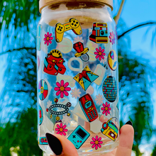 Load image into Gallery viewer, A 16oz BPA-free glass cup featuring a colorful 90s-themed UVDTF wrap with icons like Game Boys, cassette tapes, roller skates, and boomboxes. Comes with a bamboo lid and reusable glass straw, perfect for nostalgic drinkware lovers.
