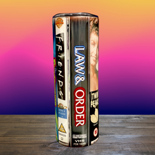 Load image into Gallery viewer, A 20 oz stainless steel insulated tumbler featuring a vinyl wrap of VHS covers from iconic &#39;90s TV shows, including Friends, The Sopranos, The Fresh Prince of Bel-Air, and Sex and the City. Comes with a lid and reusable straw, perfect for nostalgic TV lovers.
