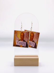 Earrings inspired by Creed Bratton from 'The Office', capturing the mischief and enigma of the show's most mysterious character. Each earring depicts the iconic 'Thief' Polaroid, symbolizing Creed's adventures and hinting at his shadowy backstory.