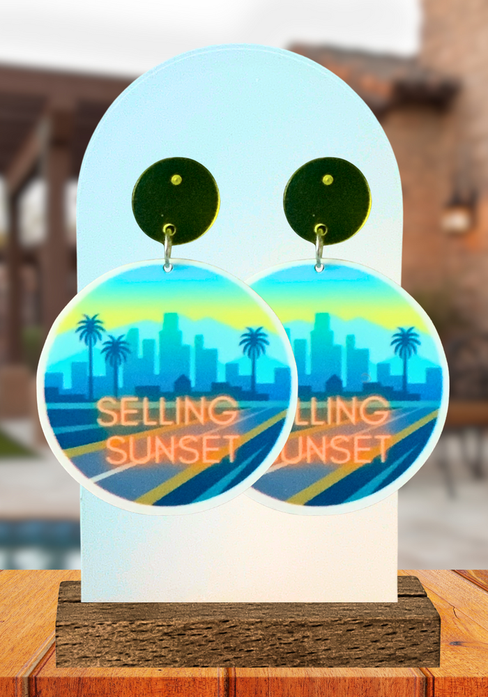 Earrings featuring the Selling Sunset logo in front of a luxurious house in the background