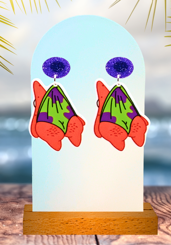 Dangling Patrick Star earrings on an earring display in front of an oceanic backdrop
