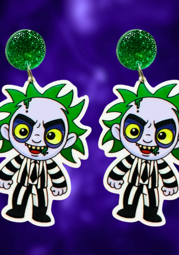 A purple background with earrings featuring a cute cartoon version of Beetlejuice, perfect for fans of the classic film and nostalgic Halloween fun.
