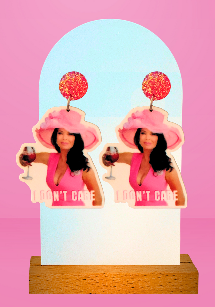 Pink background with earrings featuring Lisa Vanderpump in a pink dress and derby hat, holding a glass of rosé with the caption 