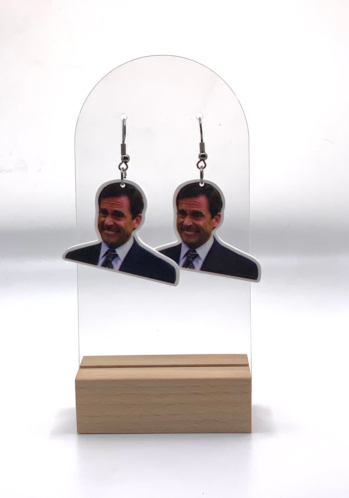 Earrings featuring Michael Scott’s memorable pained expression from the ‘Branch Closing’ episode of “The Office,” a humorous accessory for any fan of the series.