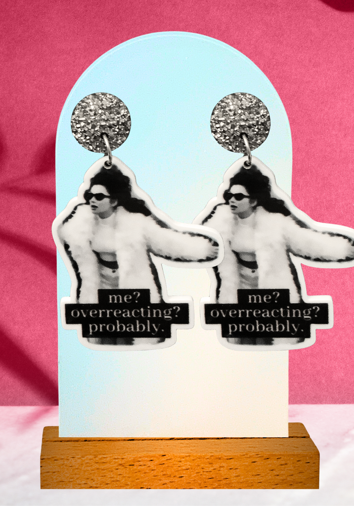 Earrings on a pink background that feature Fran Fine from the Nanny that says “me? Overreacting? Probably”
