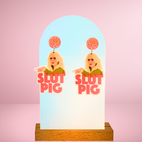 Close-up image of “Slut Pig” earrings, inspired by the iconic Real Housewives of Beverly Hills moment between Kim Richards and Brandi Glanville, perfect for Bravo reality TV fans.