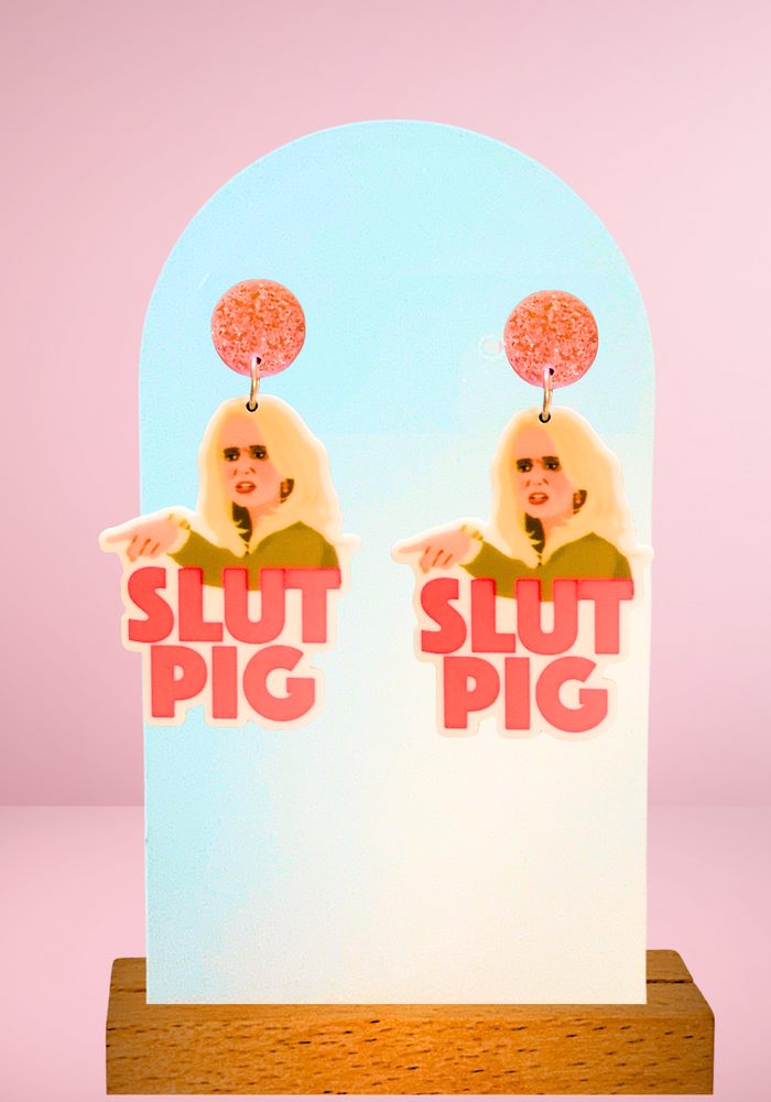 Close-up image of “Slut Pig” earrings, inspired by the iconic Real Housewives of Beverly Hills moment between Kim Richards and Brandi Glanville, perfect for Bravo reality TV fans.