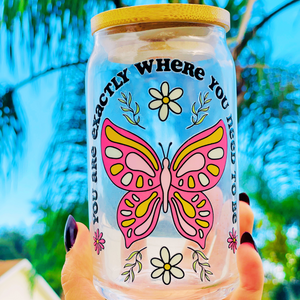 A 16 oz glass cup featuring a UVDTF wrap with a pink butterfly, daisies, and the phrase “You’re Exactly Where You Need To Be.” Comes with a bamboo lid and reusable glass straw. BPA-free and handwash only.