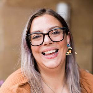 A woman smiling wearing New Girl earrings that have a photo of Jess crying and said “I just wanted to listen to Taylor Swift alone”