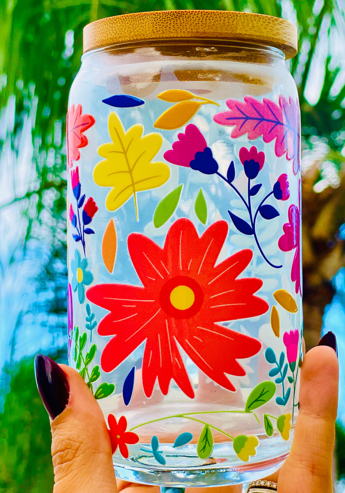 A 16 oz glass cup with a vibrant floral design featuring colorful flowers, leaves, and petals. Includes a bamboo lid and reusable glass straw, perfect for cold drinks. BPA-free, handwash only, and eco-friendly.