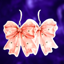 Load image into Gallery viewer, A purple background with pink coquette bow earrings with adorable ghost patterns, perfect for adding a cute and spooky twist to Halloween fashion.
