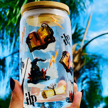 Load image into Gallery viewer, A 16 oz glass cup featuring a Harry Potter-inspired UVDTF wrap with wands, spellbooks, lightning bolts, and the Sorting Hat. Includes a bamboo lid and reusable glass straw, perfect for cold drinks. BPA-free and handwash only.
