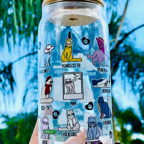 A 20 oz glass cup featuring colorful cat illustrations and Taylor Swift album-inspired designs, with the phrase 