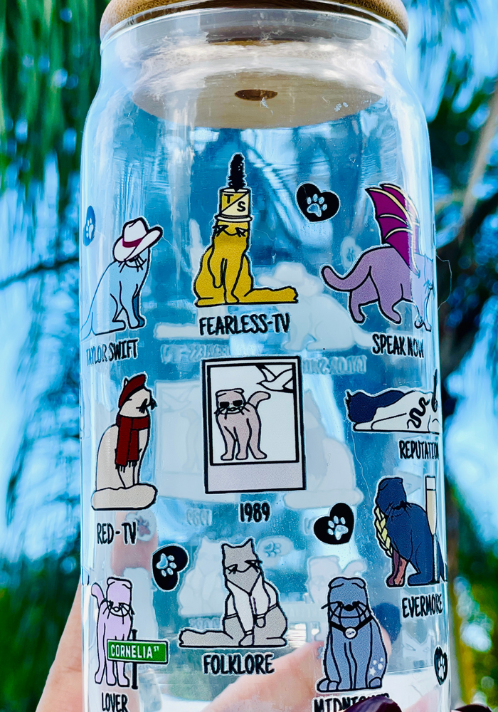 A 20 oz glass cup featuring colorful cat illustrations and Taylor Swift album-inspired designs, with the phrase 