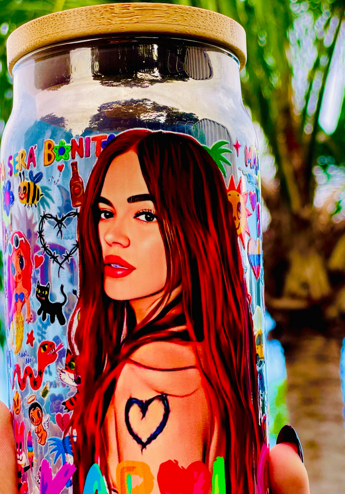 A 16 oz glass cup with a colorful Karol G-inspired UVDTF wrap featuring vibrant symbols, designs, and playful details. Includes a bamboo lid and reusable glass straw, perfect for cold drinks. BPA-free and handwash only.
