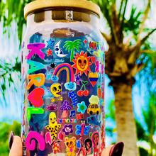 Load image into Gallery viewer, A 16 oz glass cup with a colorful Karol G-inspired UVDTF wrap featuring vibrant symbols, designs, and playful details. Includes a bamboo lid and reusable glass straw, perfect for cold drinks. BPA-free and handwash only.
