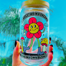 Load image into Gallery viewer, A 20 oz glass cup with a vibrant flower design that reads &quot;Manifesting My Dreams, Minding My Own Business,&quot; complete with a bamboo lid and reusable glass straw. Perfect for cold drinks and positivity fans.

Because manifesting your dreams should look as good as it feels. 🌸
